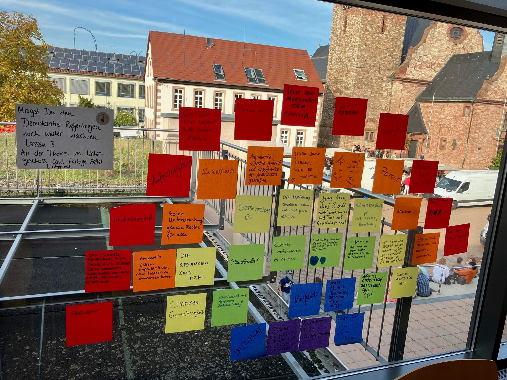 Post-Its wie ein Regenbogen angeordent auf einer Scheibe. Die Zettel sind beschriftet.